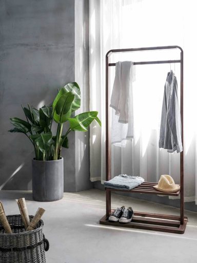 Clothing rack with garments, a hat, and a potted plant in a minimalist interior setting.