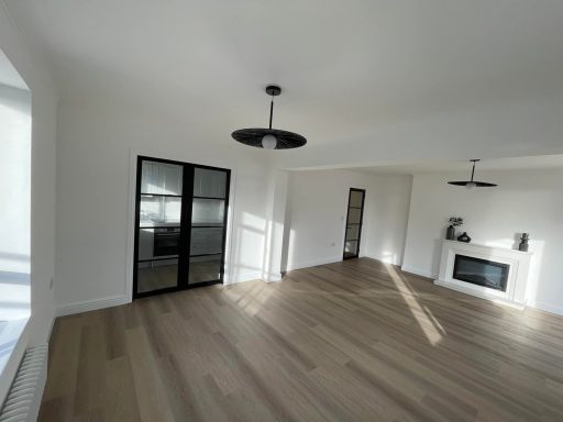 Spacious, modern room with wooden flooring, large windows, and minimal decor.