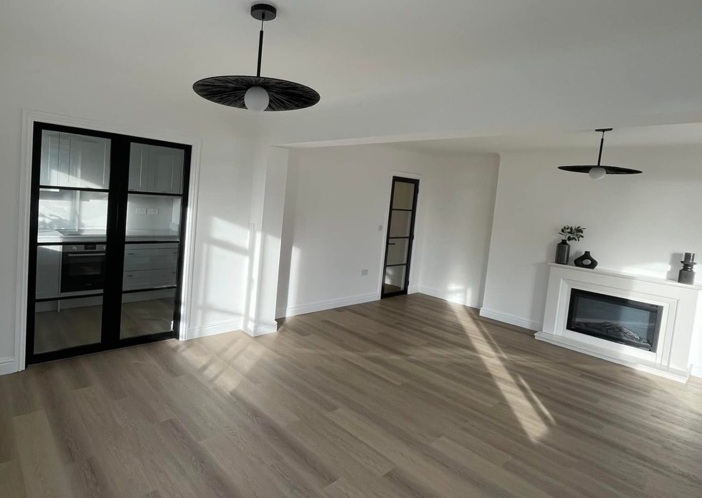 Spacious, modern living area with wooden flooring and large windows, featuring a fireplace.
