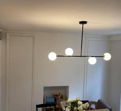 A modern ceiling light fixture with three round bulbs above a dining table.
