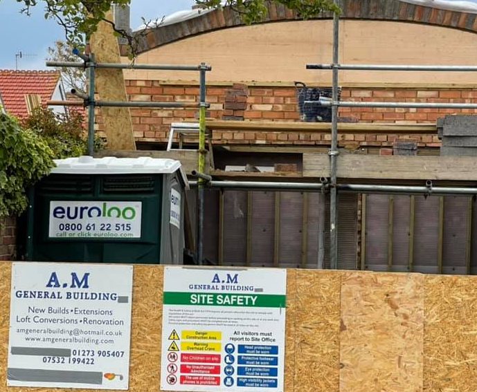 Construction site with scaffolding, signage, and a portable toilet.