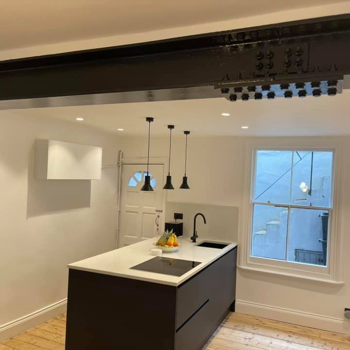 Modern kitchen and living area with large skylights, white cabinets, and a red chair. In  Brighton,Hove, Sussex area. 