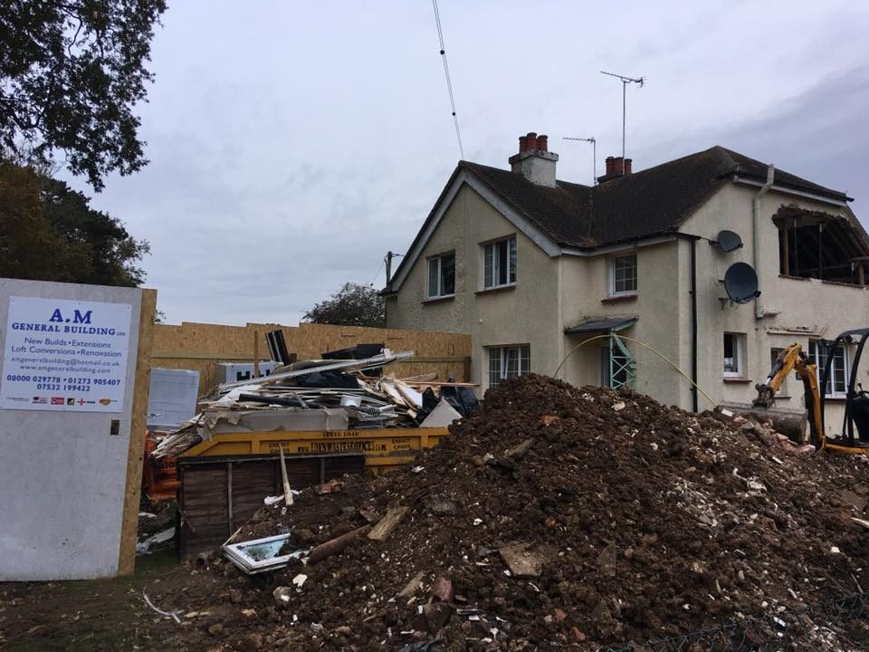 Construction site with a large mound of earth and a partially demolished house.