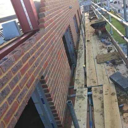 Construction site with scaffolding and wooden planks beside a brick building.