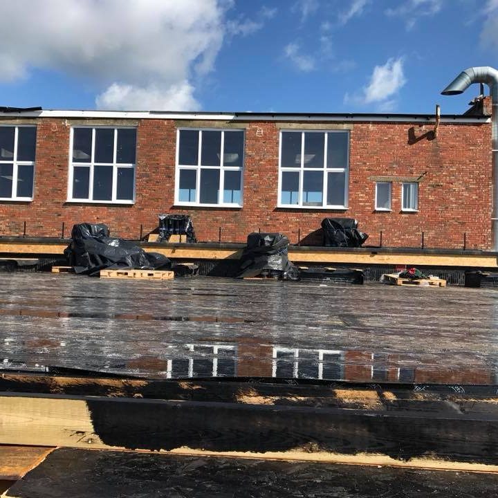 Flat roofing with construction materials and covered areas, against a brick building.