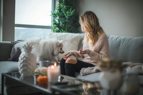 A woman sits on a sofa, interacting with a fluffy dog in a stylish living room.