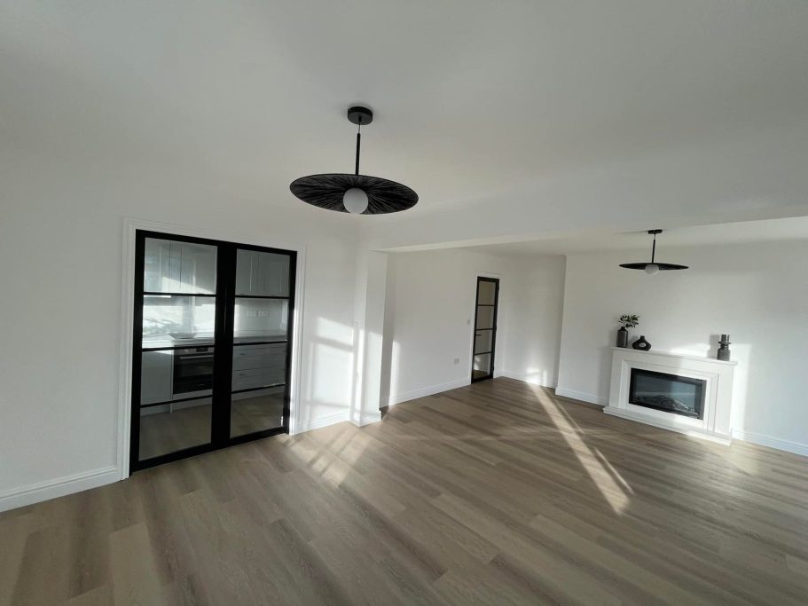 Spacious, empty living room with wooden flooring and modern lighting fixtures.