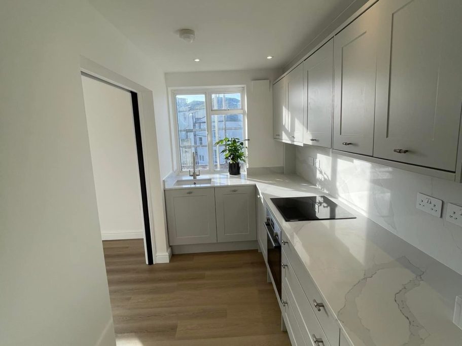 Modern kitchen with light cabinetry, a sink, and a window, featuring wooden flooring.