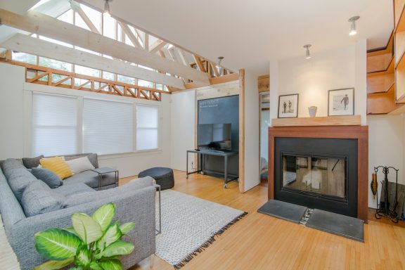 Modern living room with a grey sofa, fireplace, and wooden accents. Natural light filters in.