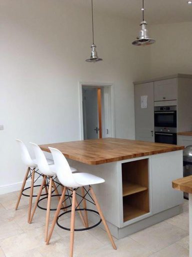 Modern kitchen with a wooden island and three white bar stools.