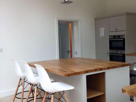 Modern kitchen with a wooden island and three white bar stools.