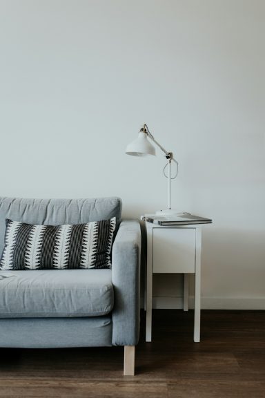 Grey sofa with striped cushions next to a white side table and lamp. Minimalist decor.